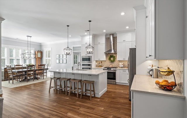 kitchen with wall chimney exhaust hood, hanging light fixtures, stainless steel appliances, a kitchen breakfast bar, and white cabinets