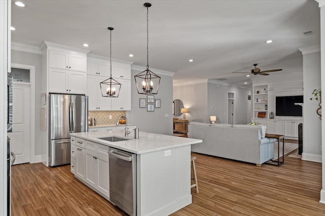 kitchen featuring ceiling fan with notable chandelier, stainless steel appliances, a kitchen island with sink, sink, and white cabinets