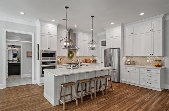 kitchen featuring pendant lighting, a kitchen island with sink, white cabinets, wall chimney range hood, and stainless steel appliances