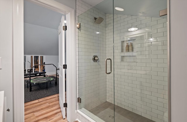 bathroom with hardwood / wood-style flooring, a shower with shower door, and vaulted ceiling