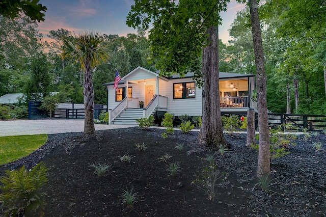 view of front of home featuring covered porch, fence, stairway, and gravel driveway