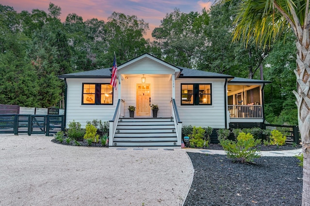 bungalow-style house featuring a porch, fence, and view of scattered trees