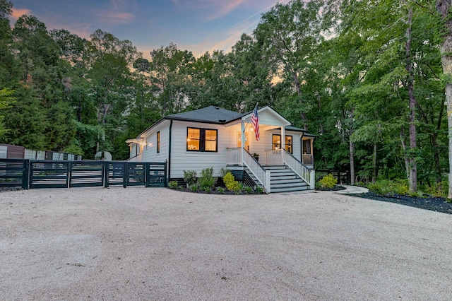 view of front of property featuring covered porch, a gate, stairs, fence, and view of scattered trees