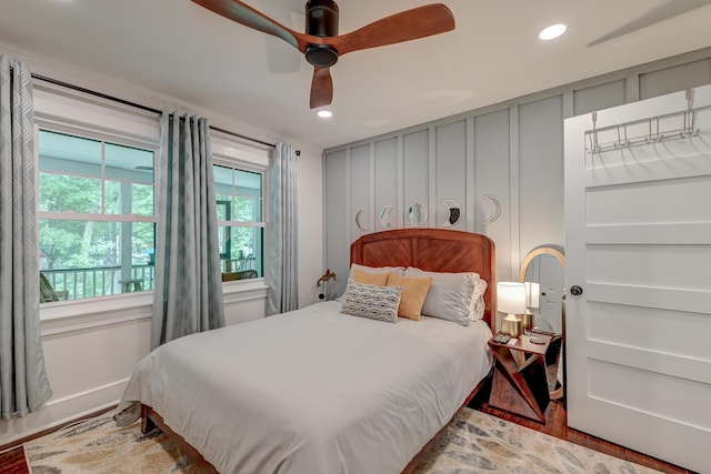 bedroom with wood finished floors, recessed lighting, ceiling fan, and a decorative wall