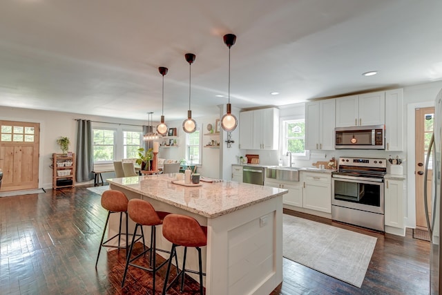 kitchen with appliances with stainless steel finishes, a sink, a kitchen island, dark wood finished floors, and recessed lighting