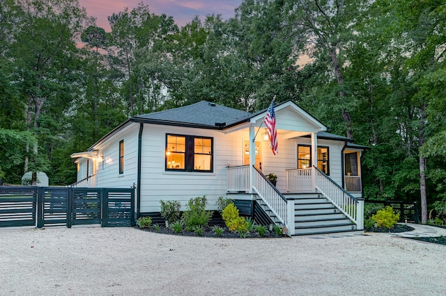 bungalow-style house with covered porch, view of wooded area, stairway, fence, and a gate