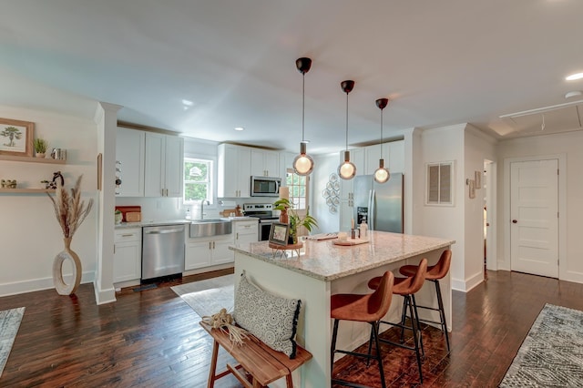 kitchen featuring appliances with stainless steel finishes, a sink, dark wood-style floors, a kitchen bar, and light stone countertops