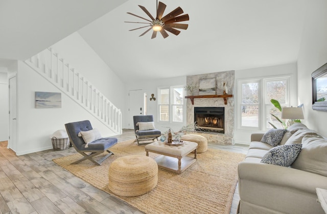 living room featuring a stone fireplace, ceiling fan, high vaulted ceiling, and light wood-type flooring