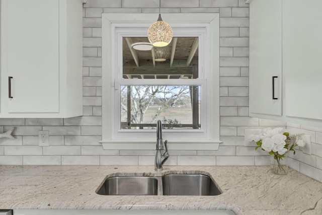 kitchen with hanging light fixtures, white cabinetry, sink, and light stone countertops