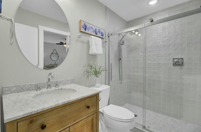 bathroom with ceiling fan, a shower with door, vanity, and toilet