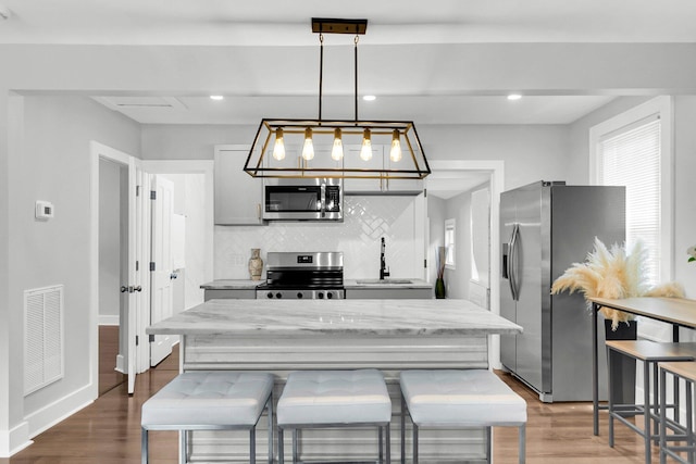 kitchen featuring appliances with stainless steel finishes, pendant lighting, tasteful backsplash, wood-type flooring, and sink