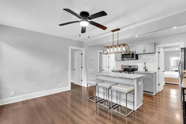 kitchen with sink, appliances with stainless steel finishes, dark hardwood / wood-style floors, light stone countertops, and decorative light fixtures