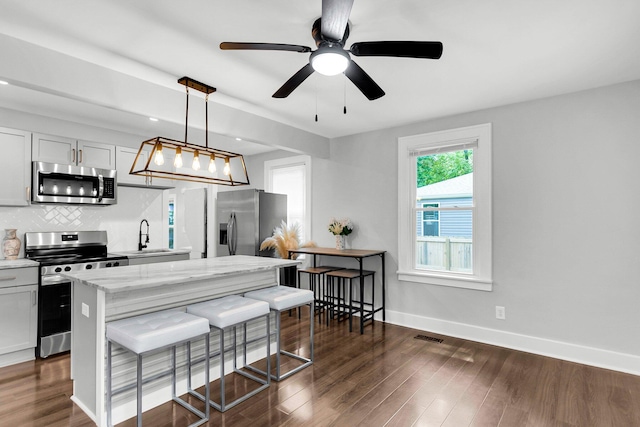 kitchen featuring appliances with stainless steel finishes, dark hardwood / wood-style floors, light stone counters, and decorative light fixtures