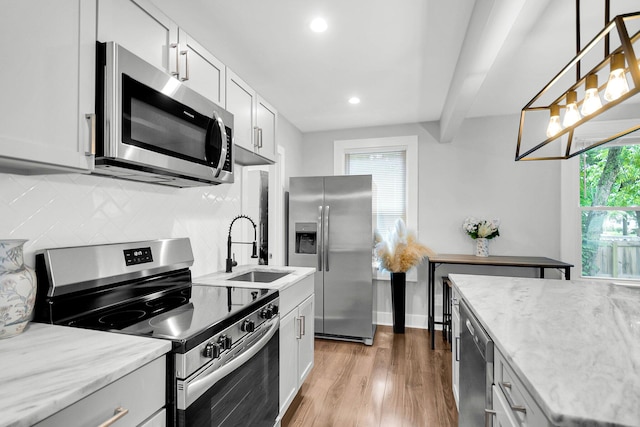 kitchen featuring pendant lighting, sink, beam ceiling, light hardwood / wood-style floors, and appliances with stainless steel finishes