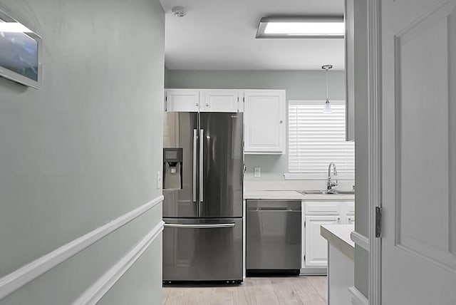 kitchen featuring pendant lighting, sink, white cabinetry, stainless steel appliances, and light hardwood / wood-style floors