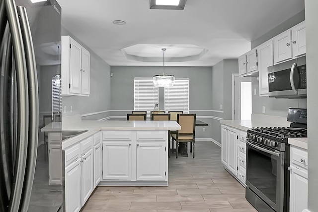 kitchen with a tray ceiling, decorative light fixtures, white cabinets, kitchen peninsula, and stainless steel appliances