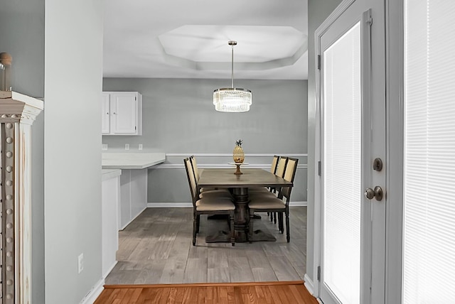 dining area with a raised ceiling and light wood-type flooring