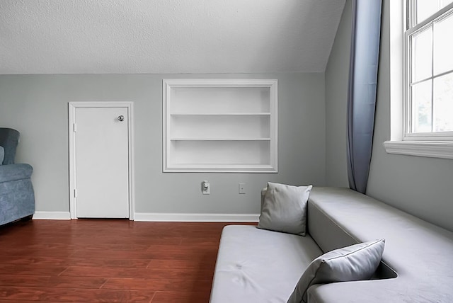 sitting room featuring built in shelves, dark wood-type flooring, and a textured ceiling