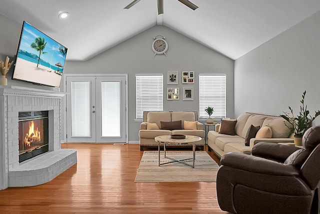 living room with vaulted ceiling, a fireplace, ceiling fan, light hardwood / wood-style floors, and french doors