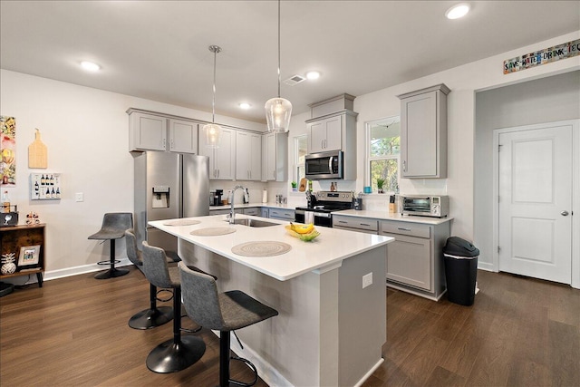 kitchen with sink, dark hardwood / wood-style flooring, an island with sink, decorative light fixtures, and appliances with stainless steel finishes