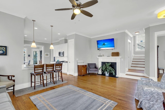 living room featuring ceiling fan, ornamental molding, and light hardwood / wood-style floors