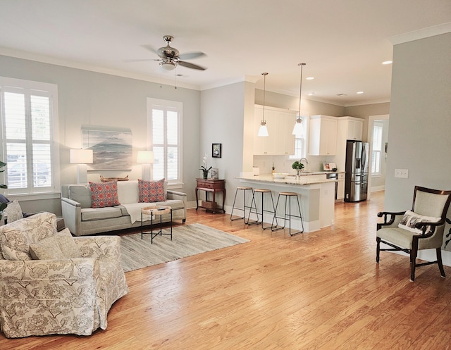 living room featuring ceiling fan, ornamental molding, light hardwood / wood-style floors, and a wealth of natural light