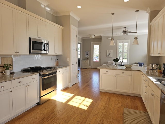 kitchen featuring ornamental molding, appliances with stainless steel finishes, kitchen peninsula, pendant lighting, and white cabinets