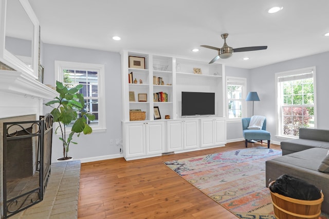 living room with baseboards, a fireplace, a ceiling fan, and light wood-type flooring