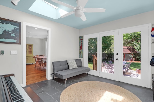 living room featuring a skylight, dark tile patterned floors, and ceiling fan