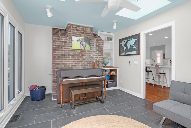 sitting room featuring dark tile patterned floors, a ceiling fan, baseboards, and a skylight