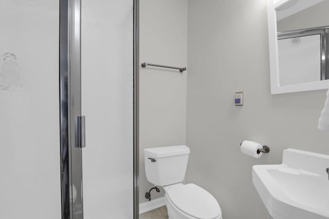 bathroom featuring tile patterned flooring, toilet, baseboards, a sink, and a stall shower