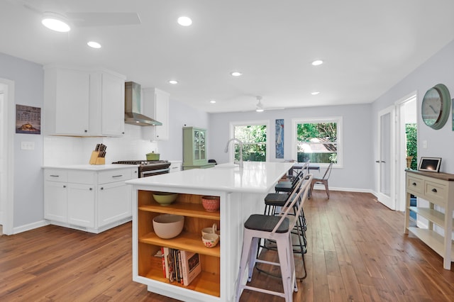 kitchen with open shelves, ceiling fan, wood-type flooring, and wall chimney exhaust hood
