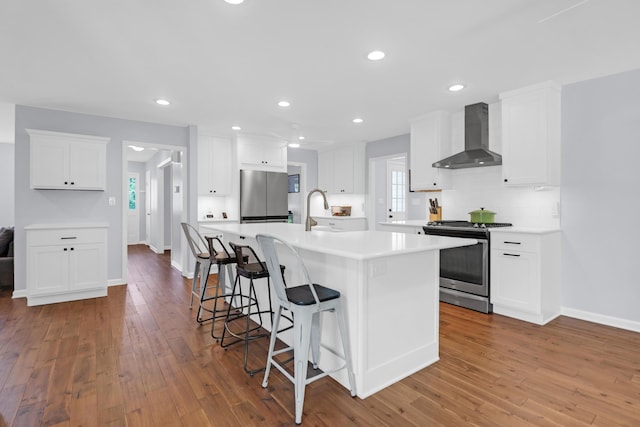 kitchen featuring a kitchen breakfast bar, white cabinetry, light countertops, stainless steel appliances, and wall chimney exhaust hood