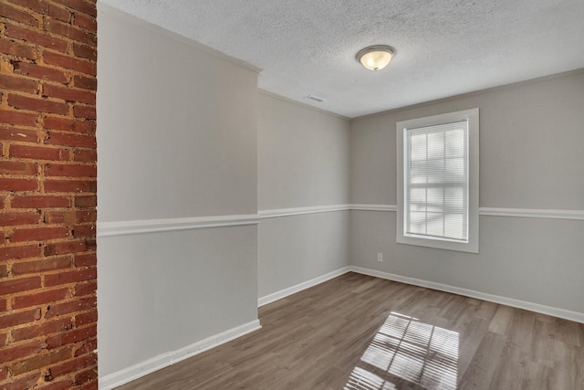 spare room with baseboards, wood finished floors, visible vents, and a textured ceiling