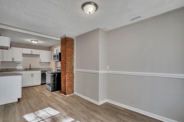 kitchen featuring light wood-style flooring, a sink, a textured ceiling, white cabinetry, and appliances with stainless steel finishes