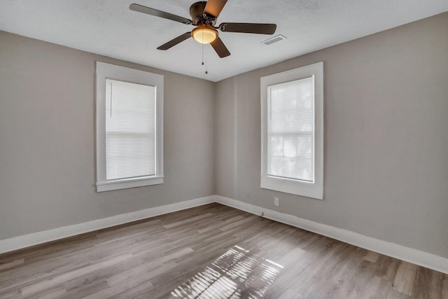 spare room with visible vents, ceiling fan, baseboards, wood finished floors, and a textured ceiling