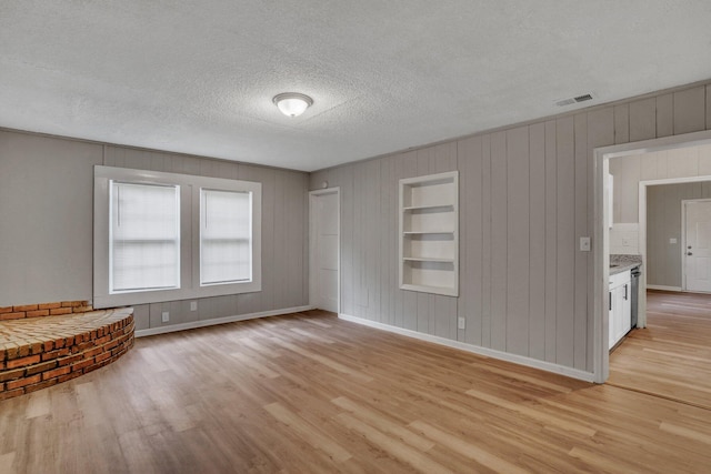 interior space featuring visible vents, baseboards, built in features, light wood-type flooring, and a textured ceiling