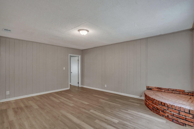 unfurnished room with a textured ceiling, visible vents, light wood-type flooring, and baseboards