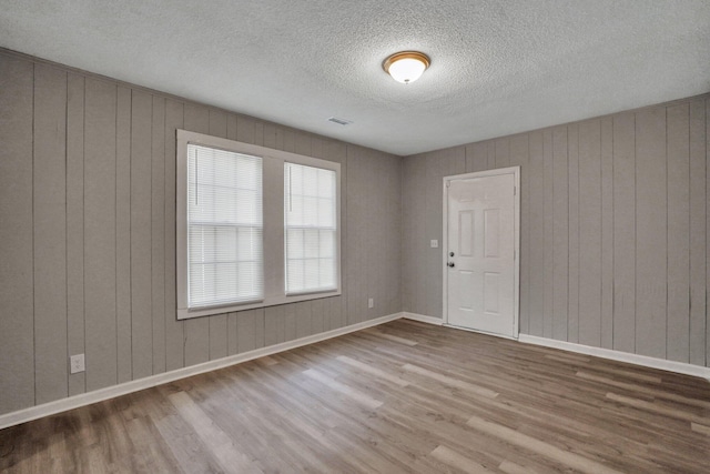 spare room featuring a textured ceiling, wood finished floors, visible vents, and baseboards