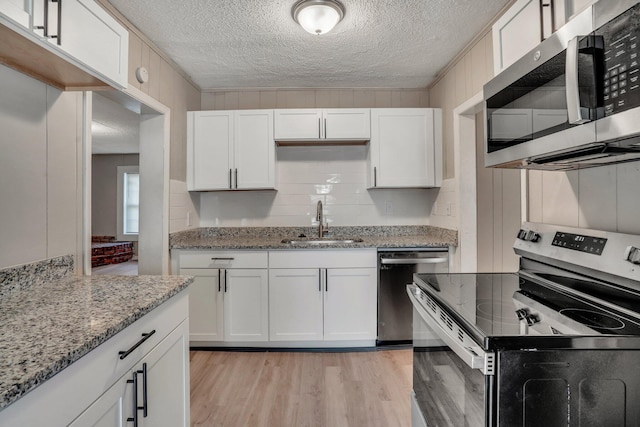 kitchen featuring light wood finished floors, light stone counters, appliances with stainless steel finishes, white cabinetry, and a sink