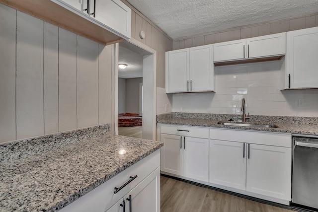 kitchen featuring a sink, light stone counters, a textured ceiling, and dishwasher