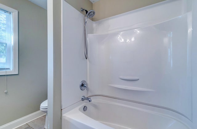 bathroom with washtub / shower combination, tile patterned flooring, baseboards, and toilet