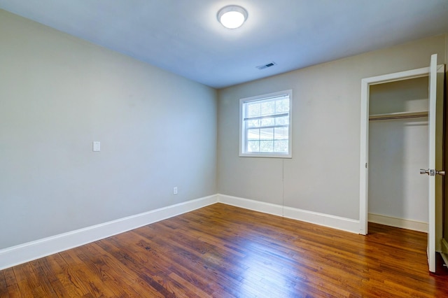 unfurnished bedroom featuring a closet, wood finished floors, visible vents, and baseboards