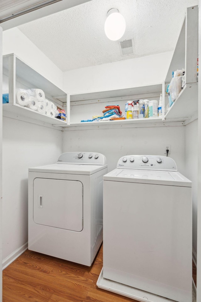 laundry room with a textured ceiling, separate washer and dryer, wood finished floors, laundry area, and baseboards