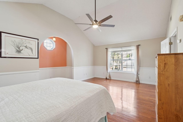 bedroom featuring arched walkways, lofted ceiling, a wainscoted wall, ceiling fan, and wood finished floors