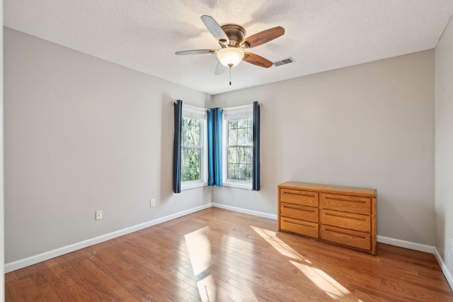 empty room with ceiling fan, wood finished floors, visible vents, and baseboards