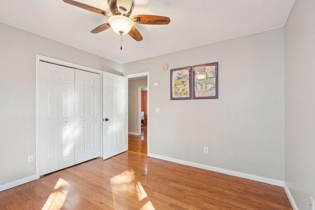 unfurnished bedroom featuring ceiling fan, a closet, light wood-style flooring, and baseboards