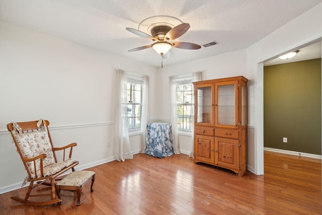 sitting room featuring light wood finished floors, visible vents, ceiling fan, a textured ceiling, and baseboards