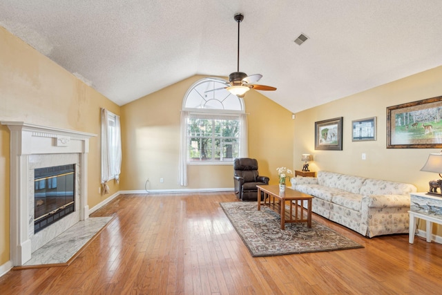 living room with a textured ceiling, hardwood / wood-style flooring, baseboards, vaulted ceiling, and a tiled fireplace