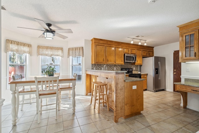 kitchen with backsplash, appliances with stainless steel finishes, brown cabinetry, a healthy amount of sunlight, and a peninsula